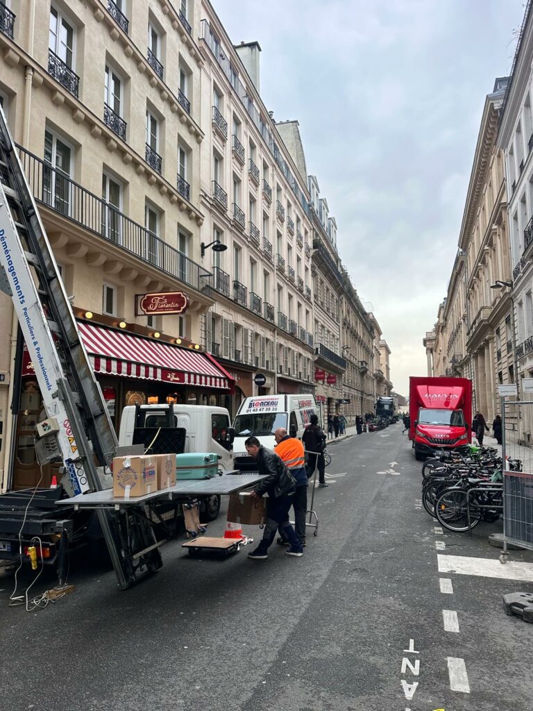 Équipe de déménageurs professionnels chargeant un plateau de monte-meuble avec des cartons et valises dans une rue de Paris.