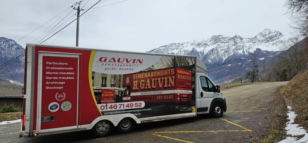 Camion de déménagement H. Gauvin rouge et blanc stationné le long d'une route avec de grandes montagnes enneigées en arrière-plan.