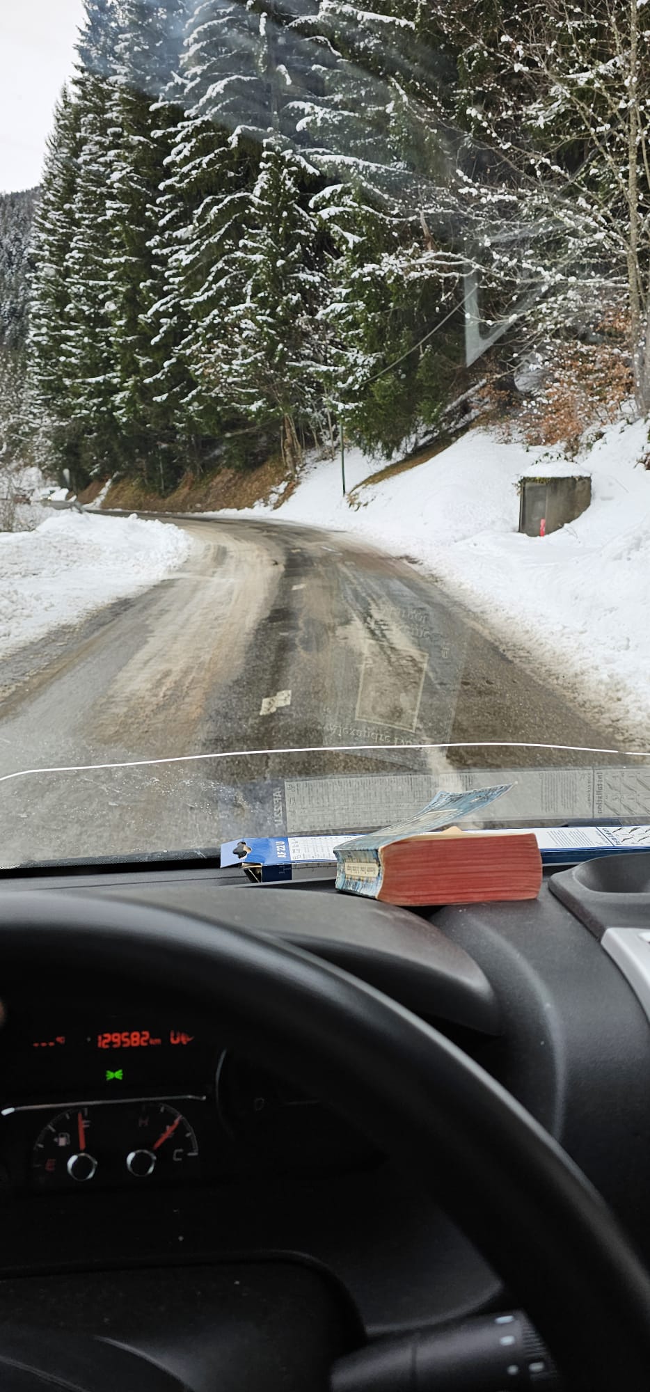 Vue depuis l'intérieur du pare-brise d'un camion de déménagement montrant une route sinueuse enneigée traversant une forêt de sapins.