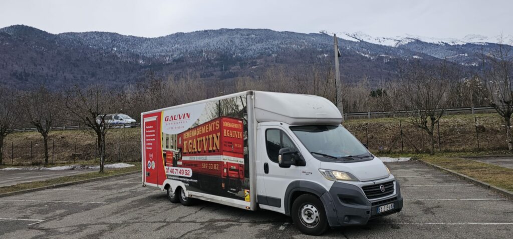 Vue de trois-quarts avant d'un camion de déménagement léger Fiat H. Gauvin stationné sur un parking face à des montagnes boisées et enneigées.