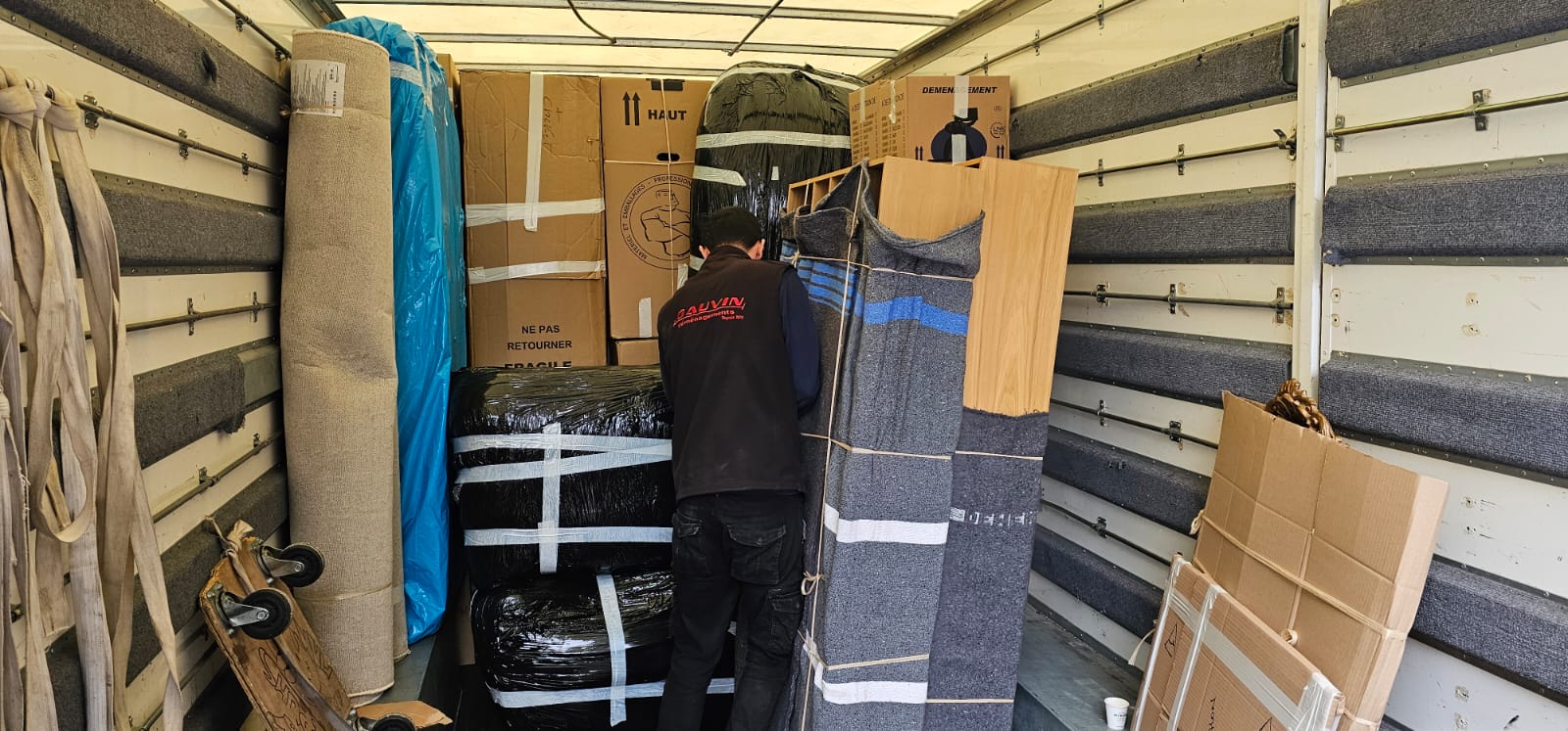 Intérieur d'un camion de déménagement capitonné H. Gauvin, montrant l'agencement optimisé des meubles protégés, des tapis et des cartons de transport.