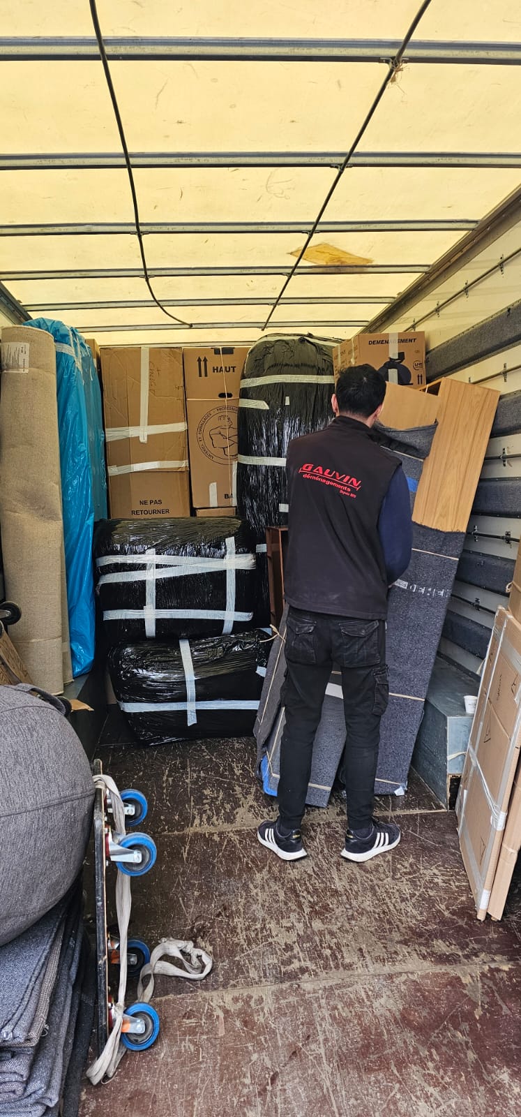 Un déménageur de l'entreprise H. Gauvin vu de dos en train de charger et caler des meubles protégés par des couvertures et des cartons à l'intérieur d'un camion de déménagement.