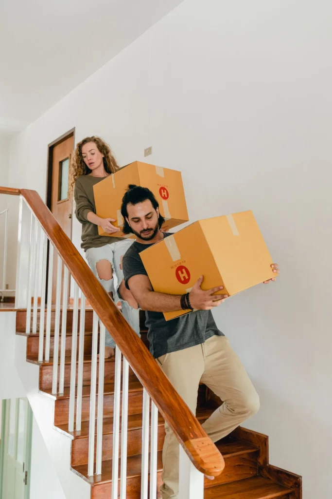Couple descendant des cartons de déménagement dans l'escalier de la maison